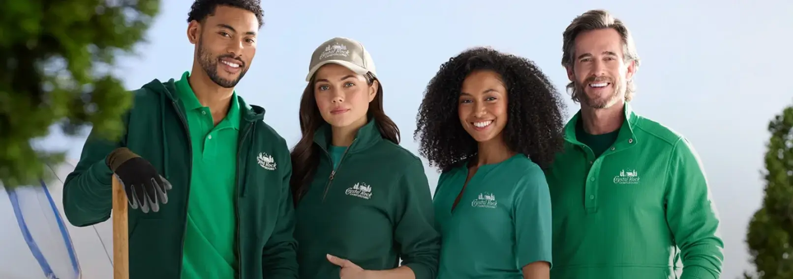 Four smiling employees in coordinated green branded uniforms representing a consistent employee uniform program